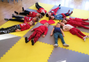 Widok na dzieci leżące na plecach wokół dużego, czerwonego serca.